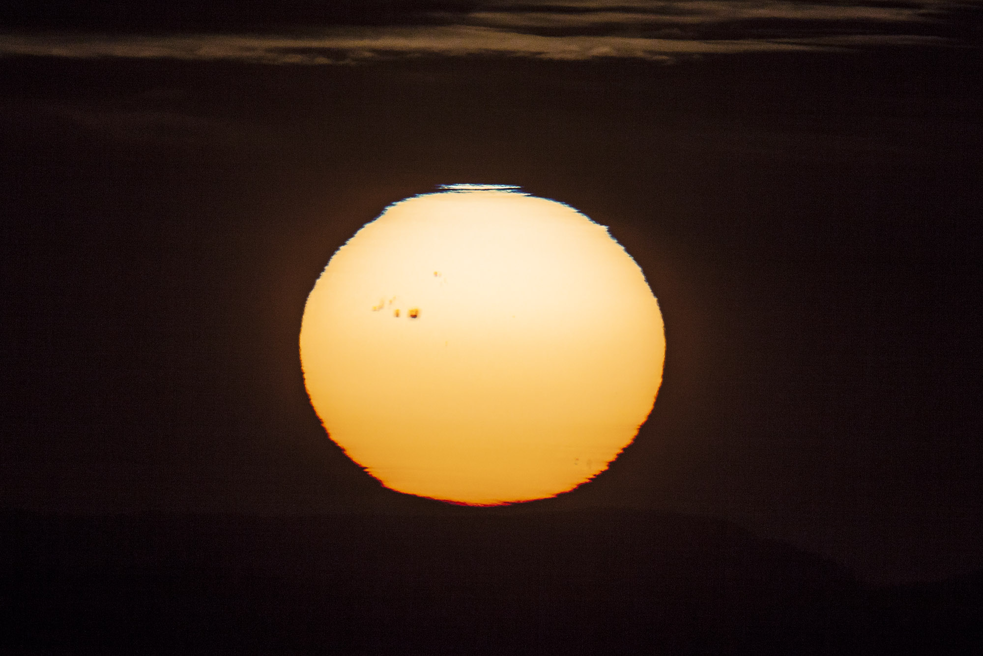 Un immense groupe de taches sombres macule la surface du Soleil, photographiée lors du coucher de l'astre du jour. Attention, il ne faut jamais regarder directement le Soleil sans protection adaptée. © Jürg Alean