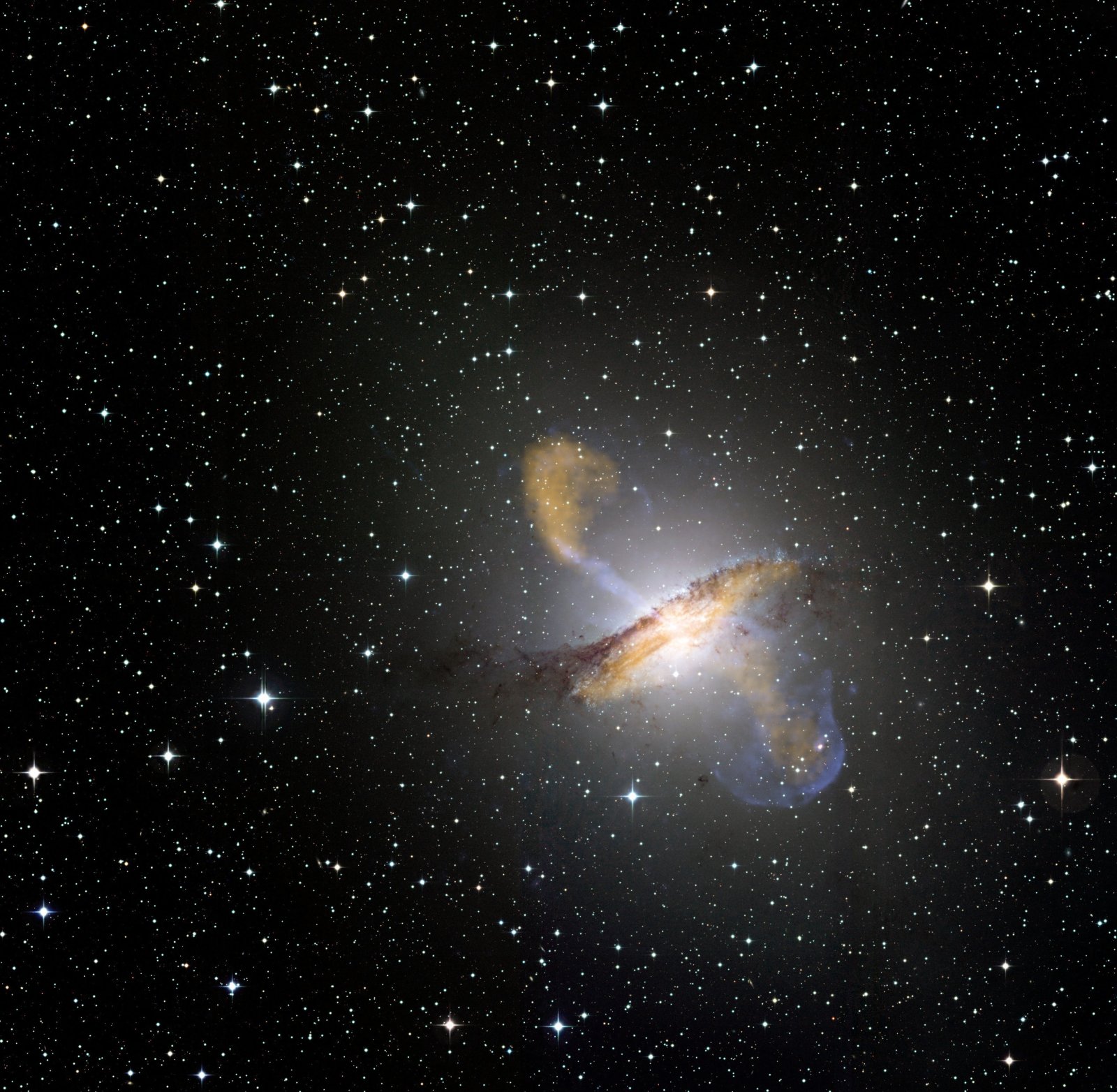 Une image de Centaurus A, révélant les jets émis par le très actif trou noir central de la galaxie. Ceci est une image composite obtenue avec trois différents instruments, fonctionnant à différentes longueurs d'onde. Les données submillimétriques à 870 microns de l’instrument Laboc sur Apex sont montrées en orange. Les données aux rayons X de Chandra sont montrées en bleu. Les données de lumière visible du Wide Field Imager (WFI) du télescope MPG-ESO de 2,2 mètres situé à La Silla, au Chili, montrent les étoiles et la ligne de poussières caractéristique de la galaxie quasiment en couleurs « réelles ». © ESO, Nasa 