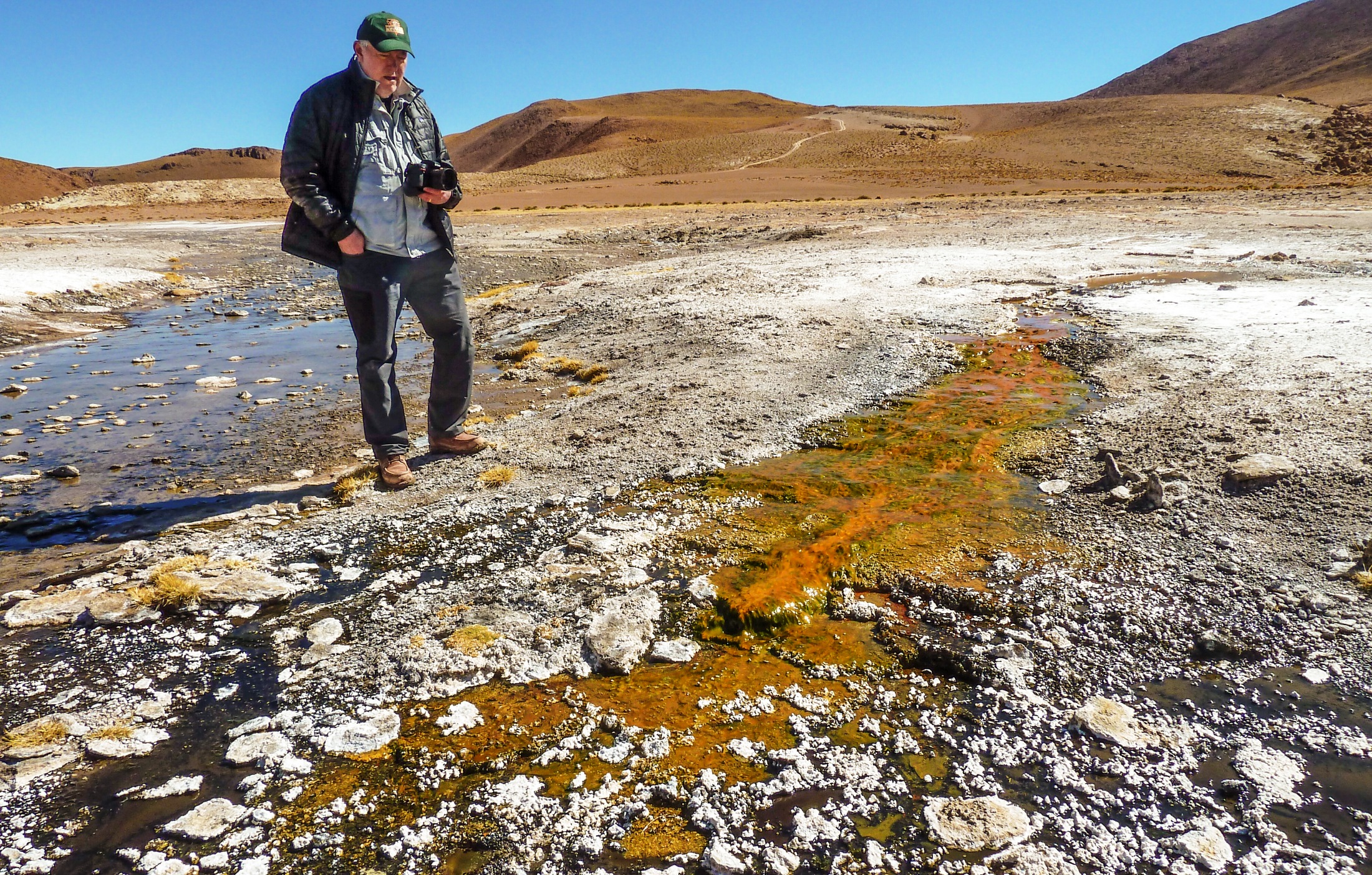 L'exobiologiste Jack Farmer inspecte un écoulement issu d'une des sources chaudes d'El Tatio au Chili. Il est coloré par la présence de micro-organismes. L'air est particulièrement sec et la température descend en dessous de zéro chaque nuit en ce lieu en altitude dans la Cordillère des Andes. Le rayonnement ultraviolet y est aussi plus intense, ce qui fait de ce lieu du désert de l'Atacama l'environnement le plus proche sur Terre de ce qu'ont dû être certaines sources chaudes martiennes. © Steve Ruff
