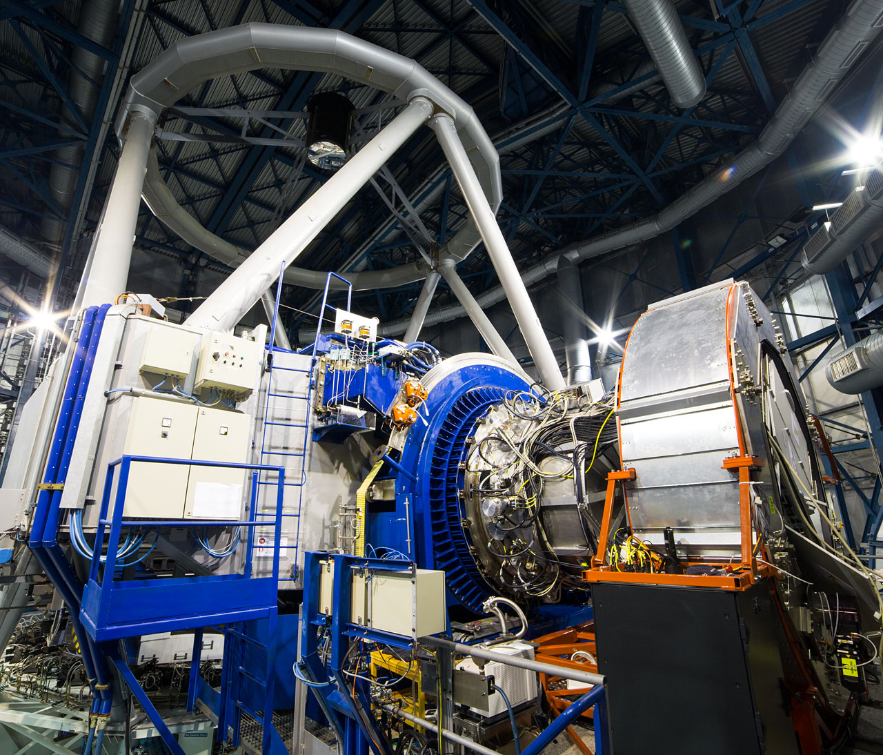 L'instrument KMos installé au foyer du Very Large Telescope (VLT) de l'ESO à l'observatoire de Paranal au Chili. Sur cette image, KMos est la structure argentée au centre, entourée par l'anneau bleu qui le connecte au télescope unitaire 1 du VLT, qui apparaît sur la gauche. Sur la droite, le grand cylindre argenté supporte l'ensemble de l'électronique de KMos et lui permet de tourner quand le télescope se déplace sur le ciel. © ESO, G. Lombardi