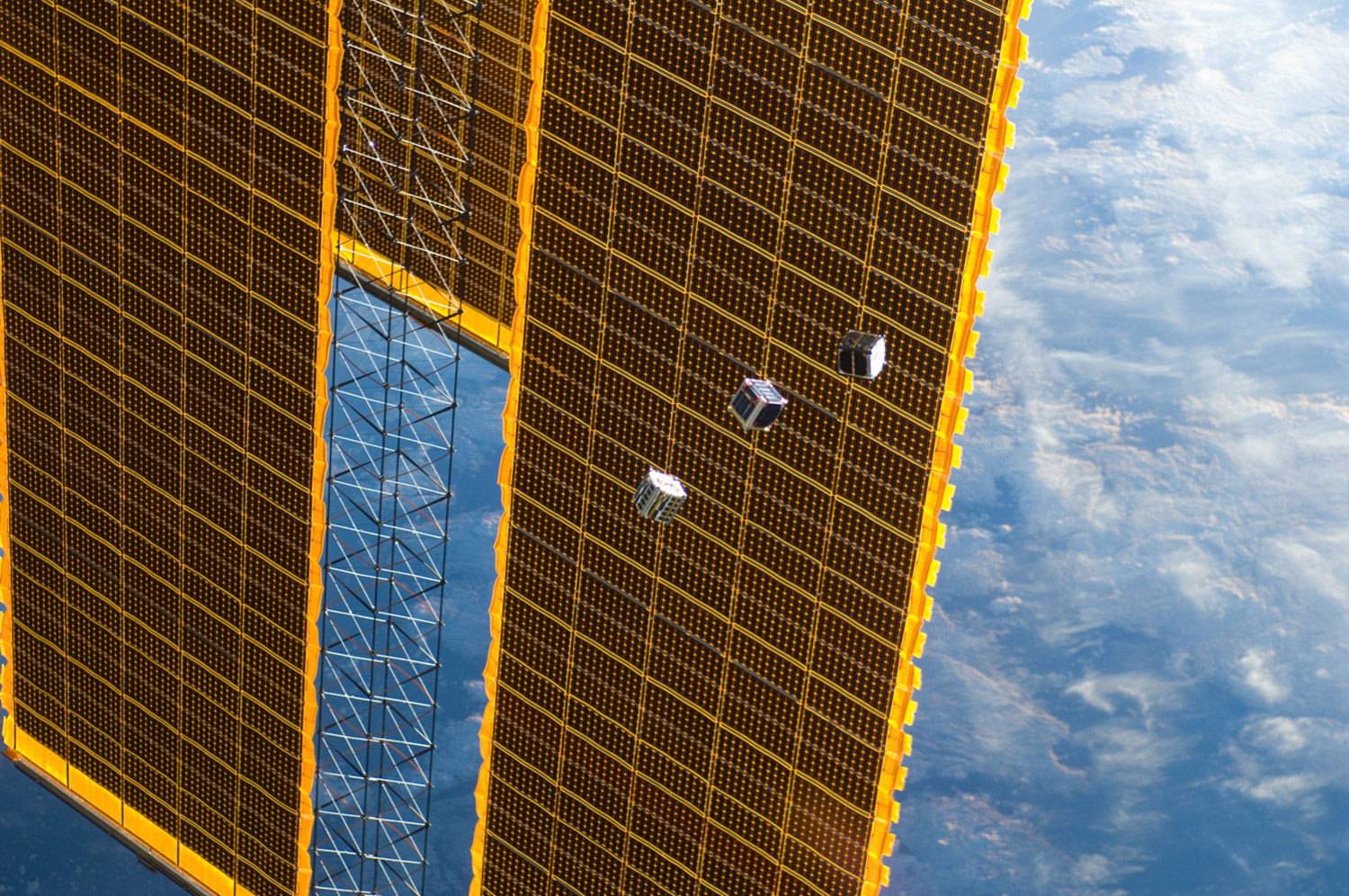 Trois des cinq petits satellites largués depuis la Station spatiale internationale, ici vus devant un des panneaux solaires de l'ISS. © Nasa