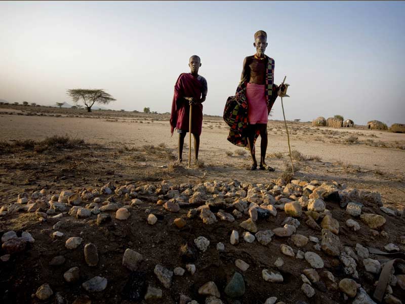 En 2011, l'Afrique de l'Est a connu une grande sécheresse. Beaucoup d'autochtones ont perdu la vie. Sur la photo, Eyanai et son grand-père Napathar se tiennent devant la tombe de la femme de Napathar, qui est décédée de malnutrition durant la sécheresse. © Kate Holt