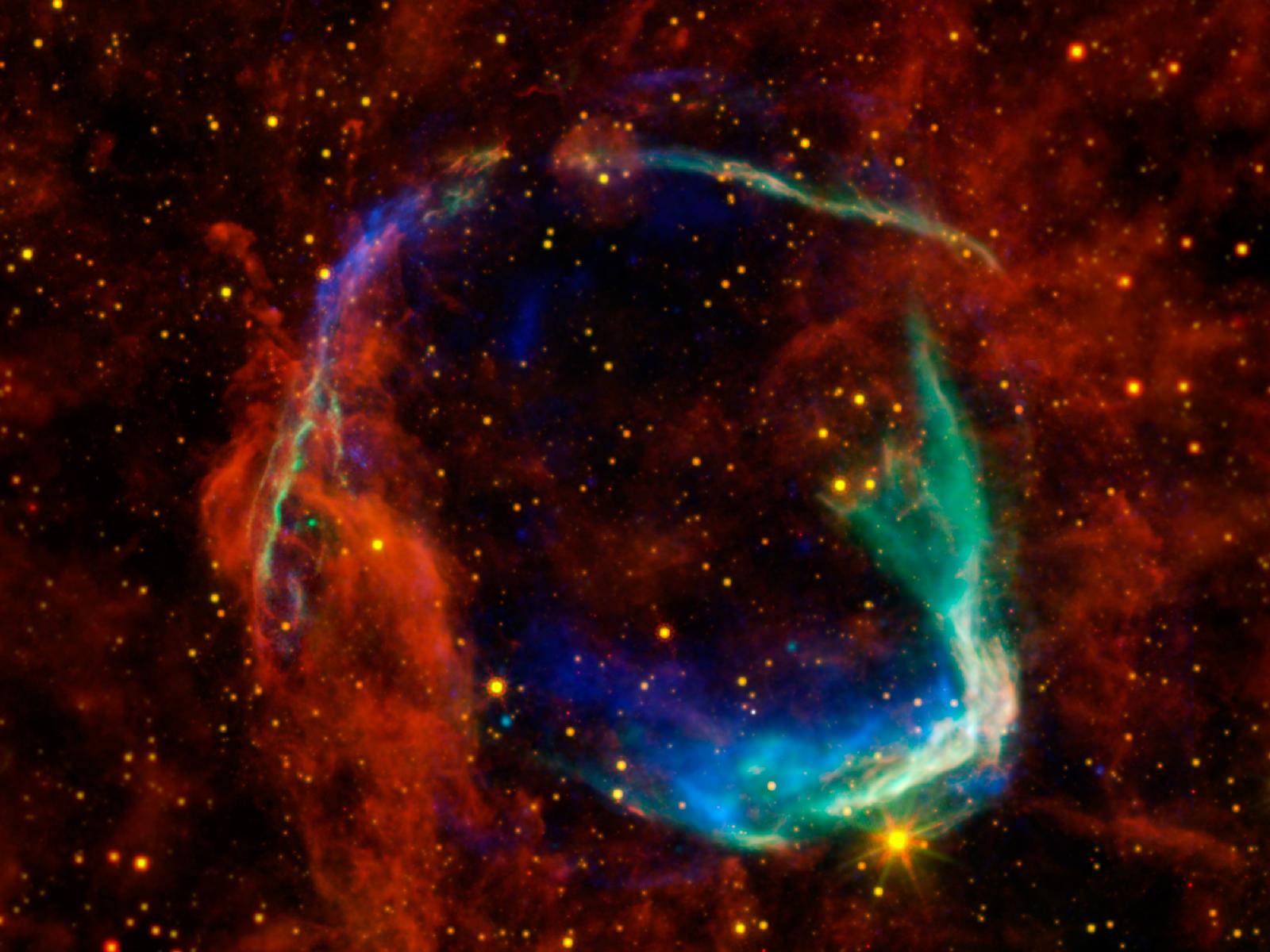 Cette image combine des données dans différentes bandes spectrales provenant de quatre télescopes spatiaux différents pour créer une vue des restes d'une supernova, appelée RCW 86, observée par les Chinois en 185. Les observations dans le domaine des rayons X de XMM-Newton (Esa) et de Chandra (Nasa) ont été combinées pour donner les détails de couleur bleu et vert. Les rayons X montrent le gaz interstellaire chauffé à des millions de degrés par le passage de l'onde de choc de la supernova. Les données infrarouges du télescope spatial Spitzer, ainsi que de Wise, sont représentées en jaune et en rouge. Elles montrent la poussière rayonnant à une température de plusieurs centaines de degrés en dessous de zéro, ce qui est plutôt chaud par comparaison à la poussière dans notre Voie lactée. © Nasa/Esa/JPL-Caltech/UCLA/CXC/SAO