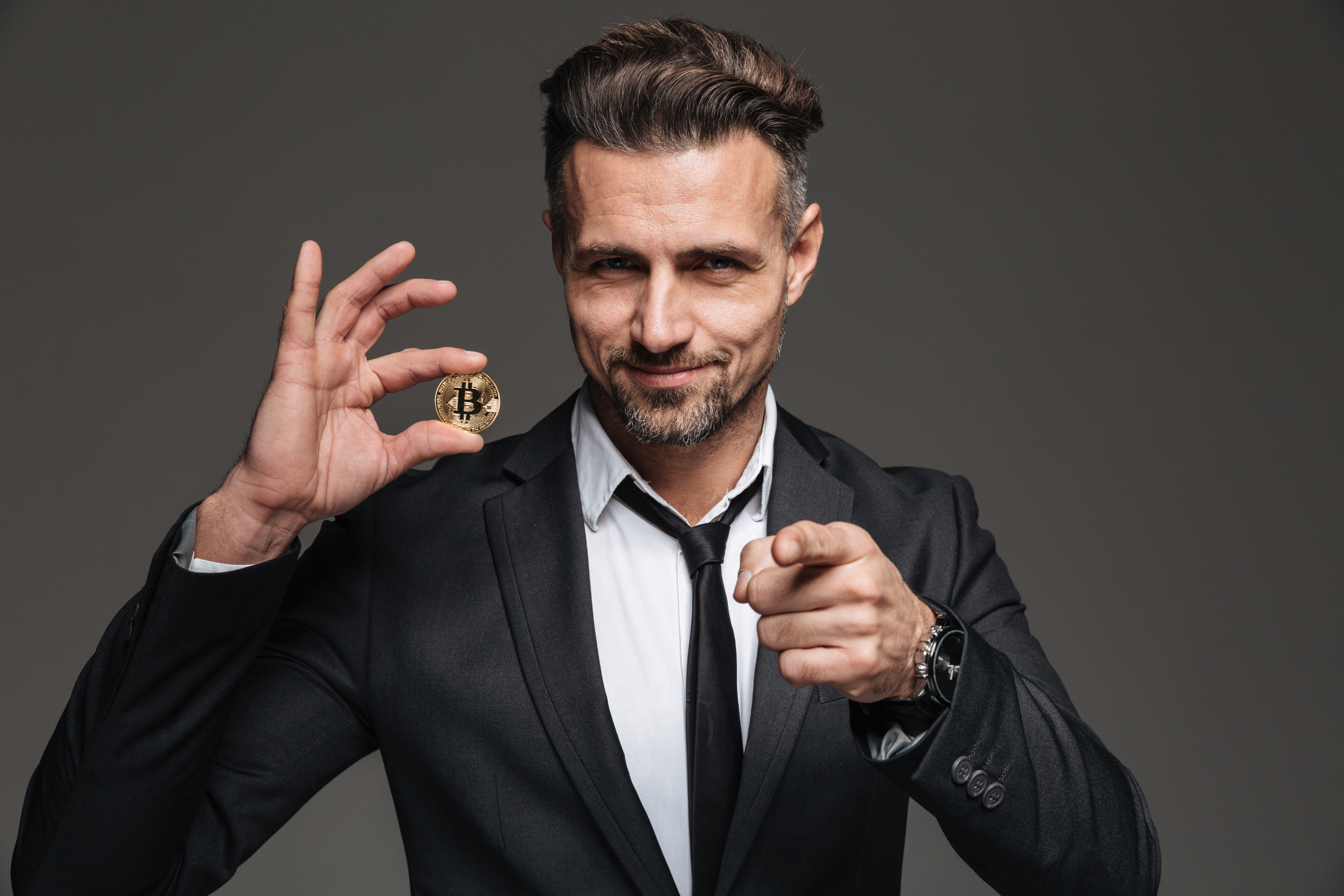 L'image d'un entrepreneur en costume et cravate qui tient un Bitcoin dans la main. © Drobot Dean