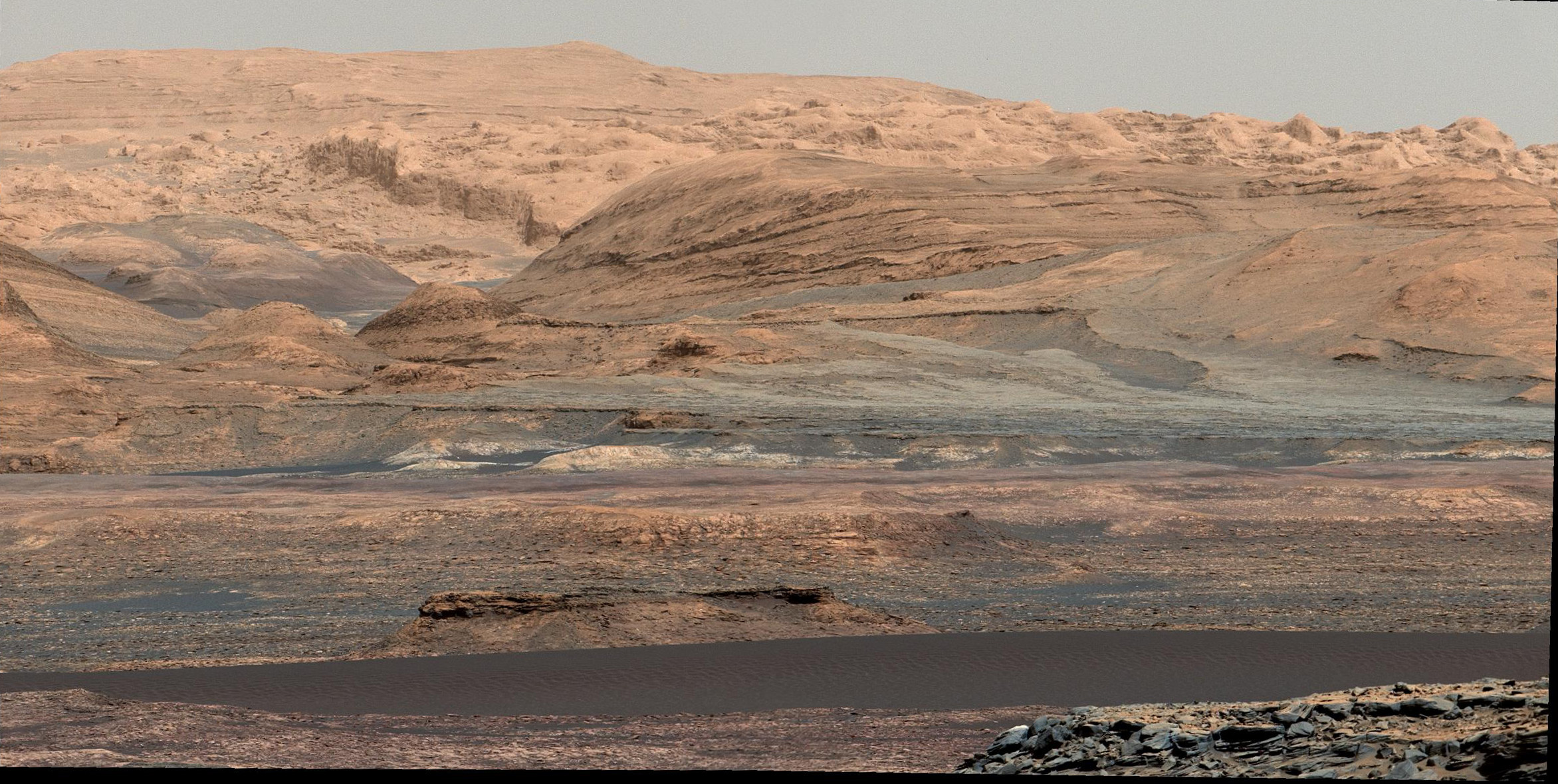 Paysage photographié par Curiosity (image mosaïque) le 25 septembre 2015 lors du Sol 1.115. La bande sombre visible dans la partie basse de l’image est une partie des dunes de Bagnold qui s’étendent le long du flanc nord-ouest du mont Sharp. Le 15 novembre, le rover n’était plus qu’à quelques dizaines de mètres de la dune n°1 qui sera la première examinée en détail sur un autre monde que la Terre. © Nasa, JPL-Caltech, University of Arizona