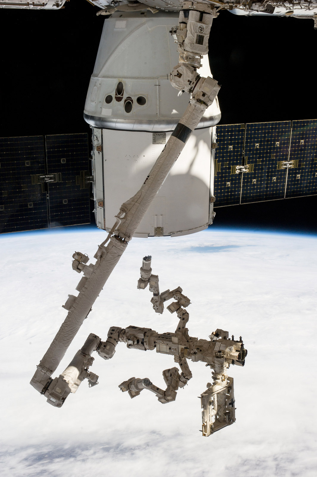 La capsule Dragon avec au premier plan le bras robotique de la Station (Canadarm 2) et, installé dessus, Dextre, s'apprêtant à extraire les deux expériences scientifiques situées à l'arrière de la capsule de SpaceX. © Nasa