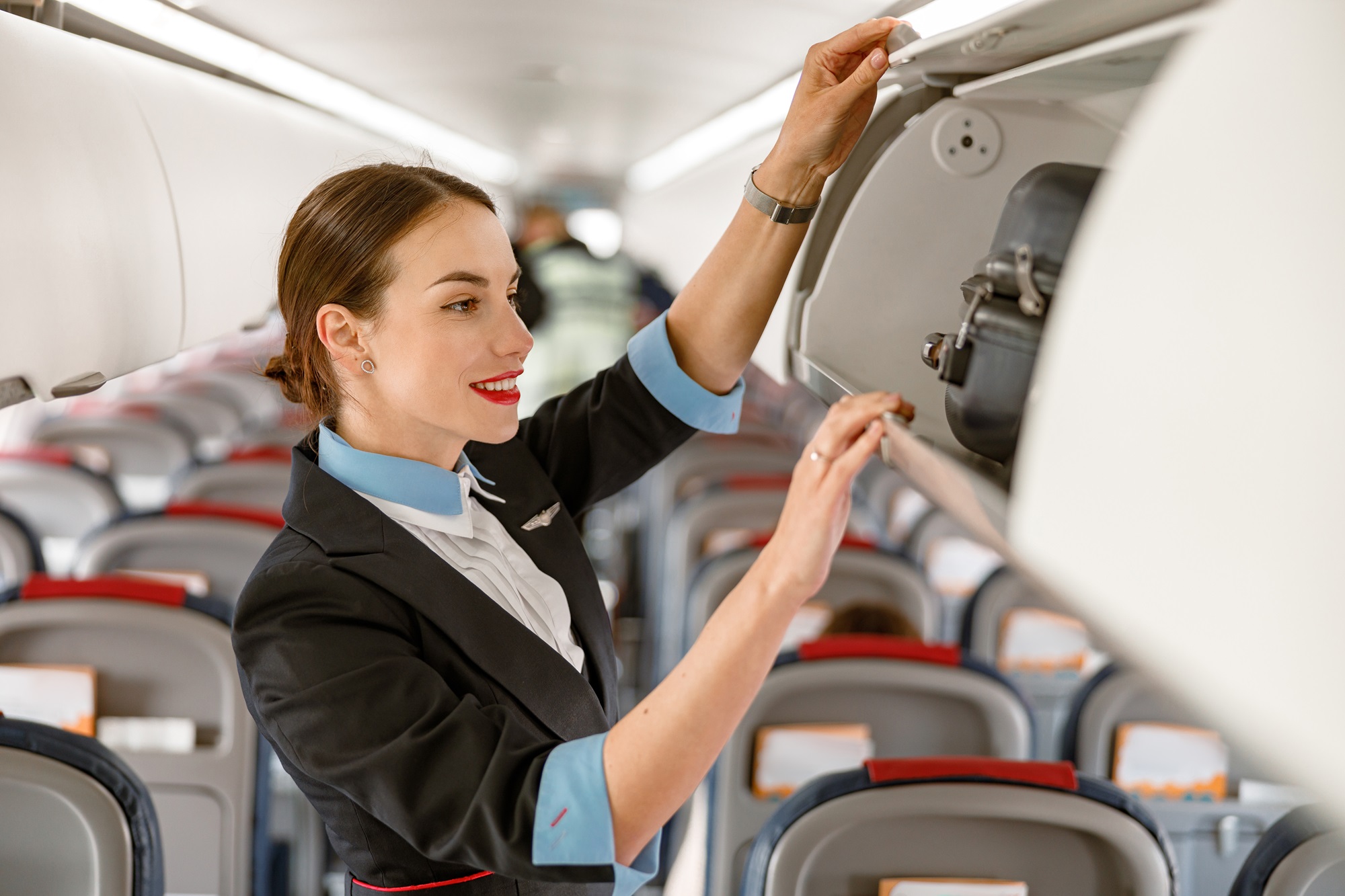 L'hôtesse de l'air veille à la sécurité et au confort des passagers à bord d'un avion. Elle vérifie les compartiments à bagages, veille au respect des consignes de sécurité et répond aux besoins des passagers. © Kostiantyn, Adobe Stock.