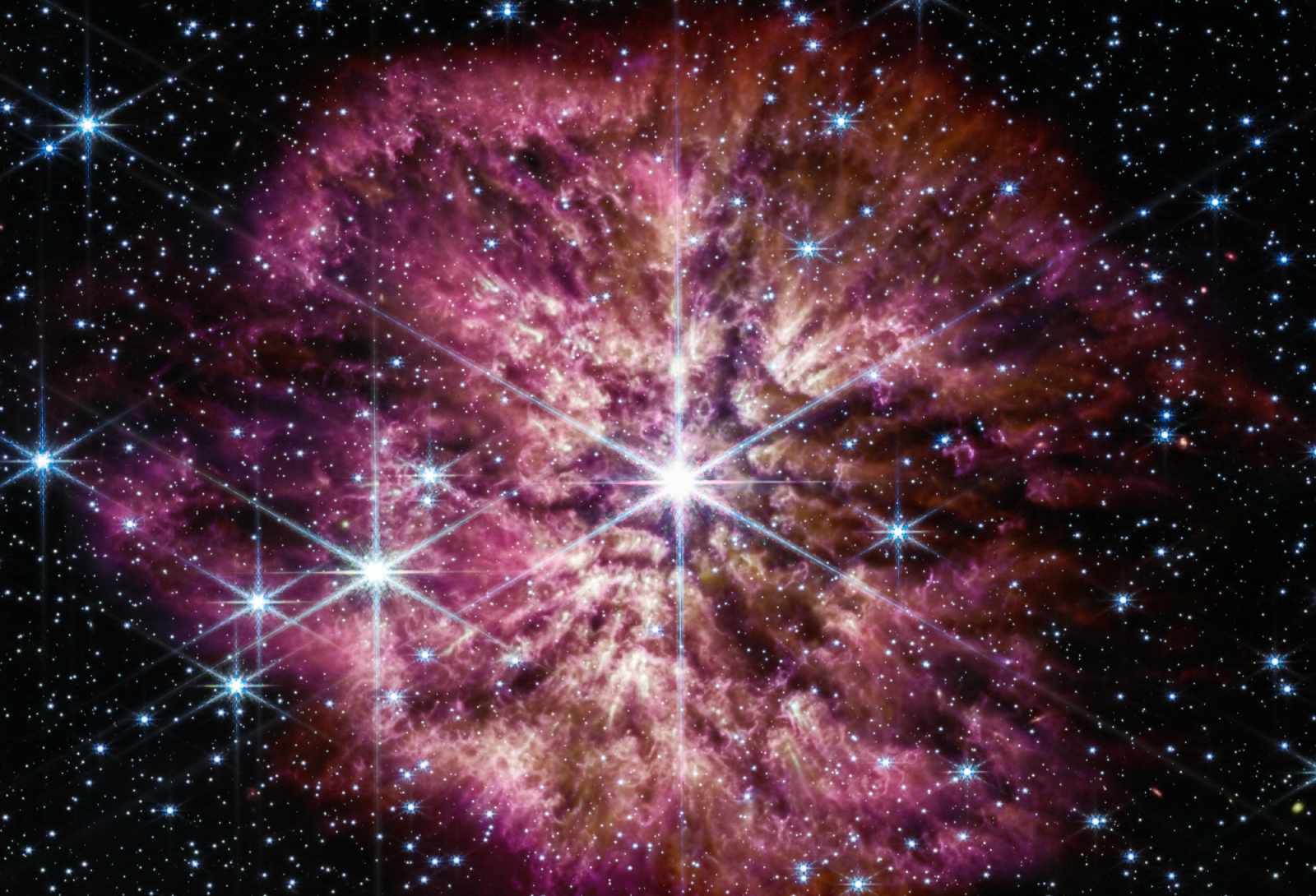 L'étoile lumineuse et chaude Wolf-Rayet 124 (WR 124) est proéminente au centre de l'image composite du télescope spatial James-Webb combinant des longueurs d'onde de lumière proche infrarouge et infrarouge moyen. L'étoile affiche les pics de diffraction caractéristiques de la caméra proche infrarouge de Webb (NIRCam), causés par la structure physique du télescope lui-même.  Les étoiles d'arrière-plan et les galaxies d'arrière-plan peuplent le champ de vision et se voit à travers la nébuleuse de gaz et de poussière qui a été éjectée de l'étoile massive vieillissante pour couvrir 10 années-lumière à travers l'espace. Une histoire des épisodes de masse passés de l'étoile peut être lue dans la structure de la nébuleuse. Plutôt que des coquilles lisses, la nébuleuse est formée d'éjections aléatoires et asymétriques. Des bouffées lumineuses de gaz et de poussière apparaissent comme des têtards nageant vers l'étoile, repoussées par le vent stellaire. © Nasa, ESA, CSA, STScI, Webb ERO Production Team